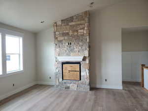 Unfurnished living room featuring a fireplace, wood-type flooring, and vaulted ceiling