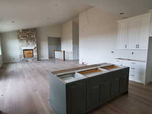 Kitchen with a kitchen island, a stone fireplace, light hardwood / wood-style floors, lofted ceiling, and white cabinets