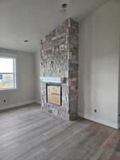 Unfurnished living room with a stone fireplace, wood-type flooring, a textured ceiling, and vaulted ceiling