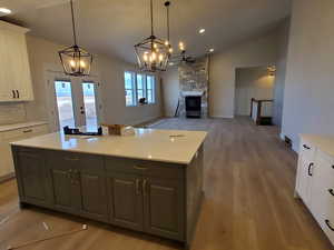 Kitchen with hanging light fixtures, vaulted ceiling, a fireplace, a kitchen island, and white cabinetry