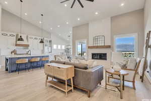 Living room with ceiling fan, sink, high vaulted ceiling, a fireplace, and light wood-type flooring