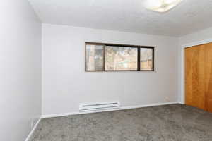 Carpeted empty room with a textured ceiling and a baseboard heating unit