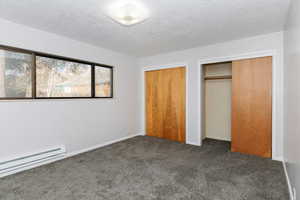 Unfurnished bedroom featuring multiple closets, a baseboard radiator, a textured ceiling, and dark carpet