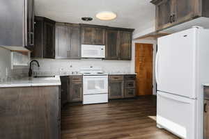 Kitchen featuring white appliances, dark brown cabinetry, dark wood-type flooring, and sink