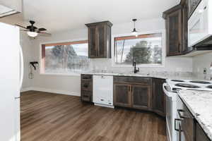 Kitchen with light stone counters, white appliances, ceiling fan, dark wood-type flooring, and hanging light fixtures