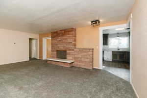 Unfurnished living room featuring a stone fireplace, sink, a textured ceiling, and dark colored carpet