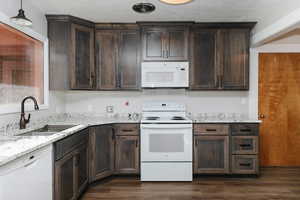 Kitchen featuring white appliances, sink, dark hardwood / wood-style floors, decorative light fixtures, and light stone counters