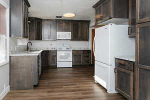 Kitchen featuring dark brown cabinets, dark hardwood / wood-style flooring, white appliances, and sink