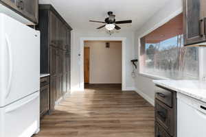 Kitchen featuring dark hardwood / wood-style flooring, white appliances, light stone counters, and dark brown cabinetry