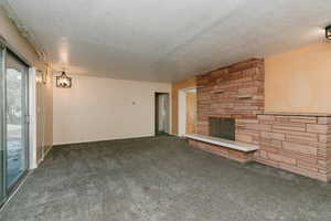 Unfurnished living room featuring a stone fireplace, dark carpet, and a textured ceiling