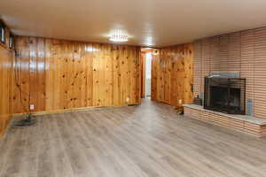 Unfurnished living room with hardwood / wood-style floors, wood walls, and a brick fireplace