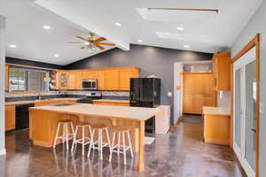 Kitchen with black appliances, a center island, lofted ceiling with skylight, and butcher block countertops