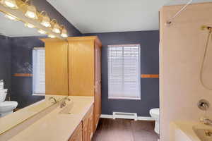 Full bathroom with baseboard heating, hardwood / wood-style floors, toilet, vanity, and bathtub / shower combination