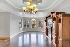 Unfurnished living room featuring an inviting chandelier, dark hardwood / wood-style flooring, crown molding, and a tray ceiling