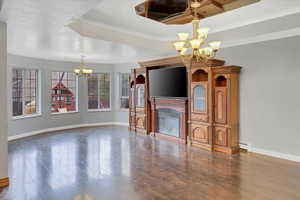 Unfurnished living room with a notable chandelier, wood-type flooring, crown molding, and a tray ceiling