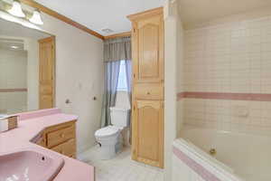 Bathroom featuring vanity, crown molding, tile patterned flooring, tiled bath, and toilet