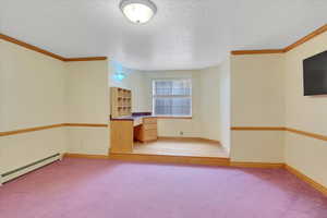 Unfurnished living room with light carpet, a textured ceiling, baseboard heating, and crown molding