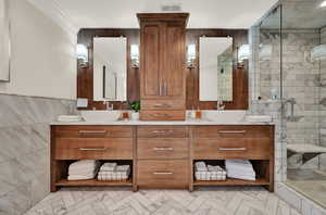 Bathroom with ornamental molding, vanity, tile walls, and a shower with shower door