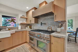 Kitchen with tasteful backsplash, light brown cabinetry, range with two ovens, and custom range hood