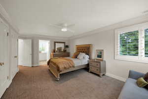 Carpeted bedroom with ceiling fan and crown molding