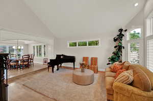 Living room featuring a chandelier, high vaulted ceiling, a healthy amount of sunlight, and light hardwood / wood-style floors