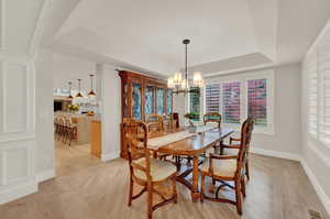 Dining room featuring a chandelier, a tray ceiling, ornate columns, and light hardwood / wood-style floors