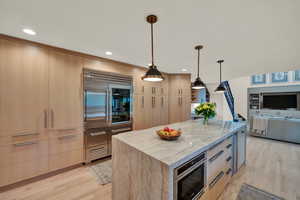 Kitchen featuring light brown cabinetry, a kitchen island, decorative light fixtures, and light wood-type flooring