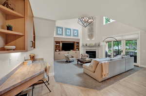 Living room with high vaulted ceiling, a chandelier, a wealth of natural light, and light hardwood / wood-style flooring