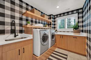 Washroom with washing machine and clothes dryer, sink, light tile patterned floors, and cabinets