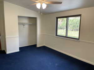 Unfurnished bedroom featuring dark colored carpet, ceiling fan, lofted ceiling, and a closet