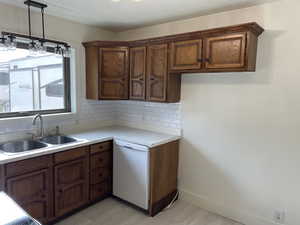 Kitchen featuring backsplash, dishwasher, sink, and pendant lighting