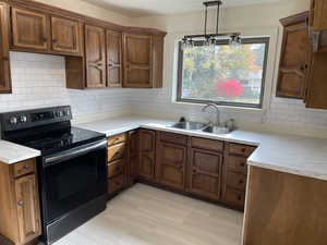 Kitchen with backsplash, black electric range, hanging light fixtures, and sink