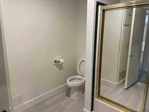 Bathroom with hardwood / wood-style flooring, toilet, and enclosed tub / shower combo