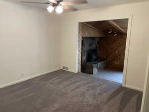 Unfurnished living room featuring ceiling fan, wood walls, a wood stove, and carpet floors