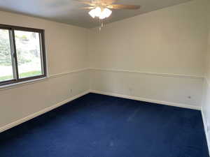 Unfurnished room featuring ceiling fan and dark carpet