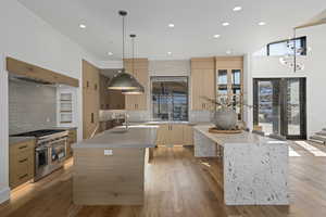 Kitchen featuring a kitchen island with sink, double oven range, decorative light fixtures, and light wood-type flooring