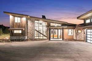 Back house at dusk featuring a garage and french doors