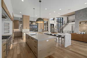 Kitchen with light wood-type flooring, ventilation hood, sink, light brown cabinets, and a large island