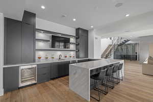 Kitchen with gray cabinetry, sink, beverage cooler, a breakfast bar, and light wood-type flooring