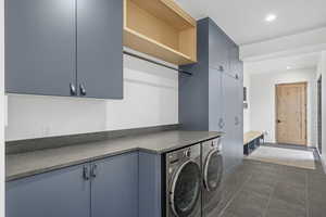 Clothes washing area with cabinets, washer and dryer, and dark tile patterned flooring