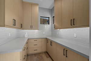 Kitchen featuring light brown cabinets, light wood-type flooring, and tasteful backsplash