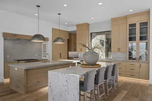 Kitchen with light brown cabinets, light hardwood / wood-style flooring, hanging light fixtures, and an island with sink