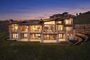 Back house at dusk with a lawn, a balcony, and a patio