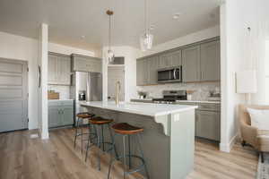 Kitchen with decorative light fixtures, light wood-type flooring, backsplash, and appliances with stainless steel finishes