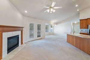 Carpeted living room with sink, ceiling fan with notable chandelier, high vaulted ceiling, and a tiled fireplace