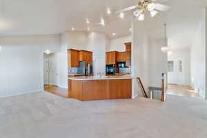 Kitchen with kitchen peninsula, light colored carpet, high vaulted ceiling, and black appliances