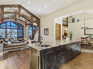 Kitchen featuring sink, pendant lighting, wood-type flooring, a center island with sink, and high vaulted ceiling