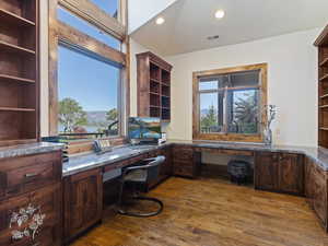 Home office with dark wood-type flooring, built in desk, and lofted ceiling