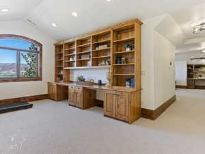 Carpeted office with built in desk and vaulted ceiling