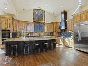 Kitchen featuring a breakfast bar area, built in appliances, light stone counters, and a center island with sink